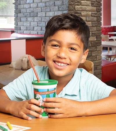 A child with a drink cup, lid and straw in a restaurant setting